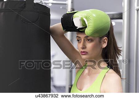 Portrait of a young woman at gym leaning against punchbag wearing boxing glove View Large Photo Image Stock Image - Portrait of a young woman at gym leaning against punchbag wearing boxing glove. Fotosearch