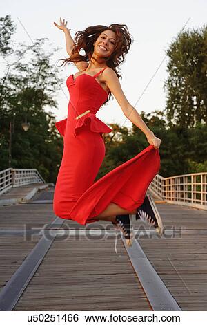 Stock Photograph - Portrait of a young woman in a smart red dress and baseball shoes jumping in motion. Fotosearch