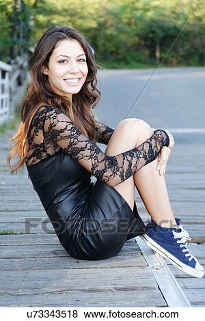 Portrait of a young woman sitting holding knees smiling at camera View Large Photo Image Stock Photo - Portrait of a young woman sitting holding knees smiling at camera. Fotosearch