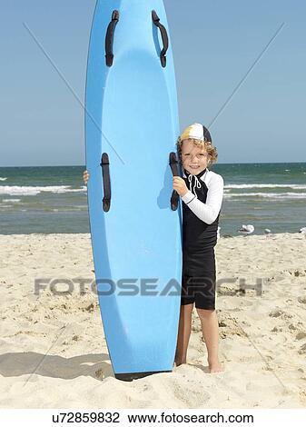 Stock Image - "Portrait of cute boy nipper (child surf life savers) next to surfboard at beach, Altona, Melbourne, Australia". Fotosearch