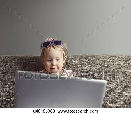 Stock Photo - Portrait of female toddler using laptop on sofa. Fotosearch
