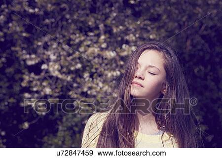 Stock Photo - Portrait of girl with eyes closed in front of foliage. Fotosearch
