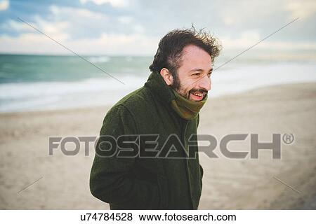 Stock Photo - "Portrait of mid adult man on windy beach, Sorso, Sassari, Sardinia, Italy". Fotosearch
