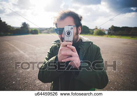 Portrait of mid adult man pointing vintage movie camera on waste ground View Large Photo Image Stock Photograph - Portrait of mid adult man pointing vintage movie camera on waste ground. Fotosearch
