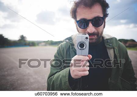 Stock Photograph - Portrait of mid adult man posing with vintage movie camera on waste ground. Fotosearch