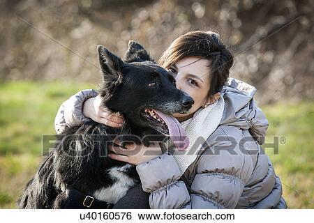 Stock Photograph - Portrait of mid adult woman kissing her dog in field. Fotosearch