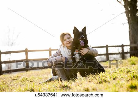 Portrait of mid adult woman sitting with her dog in field View Large Photo Image Stock Image - Portrait of mid adult woman sitting with her dog in field. Fotosearch