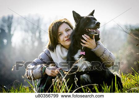 Stock Photo - Portrait of mid adult woman with arm around her dog in field. Fotosearch