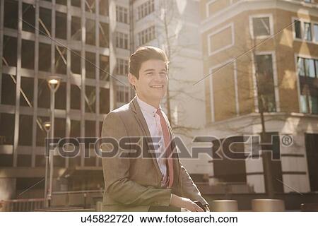 Stock Image - Portrait of young city businessman walking outside office building. Fotosearch