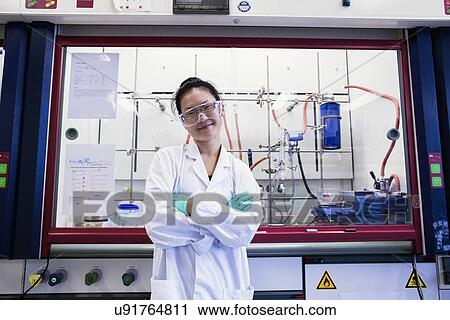 Stock Image - Portrait of young female scientist in front of fume hood in lab. Fotosearch
