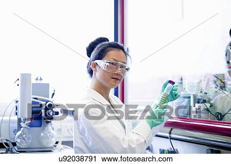 Stock Image - Portrait of young female scientist looking at sample in lab. Fotosearch