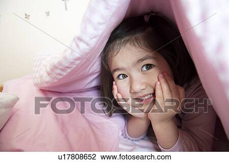 Stock Image - "Portrait of young girl, hiding under duvet". Fotosearch