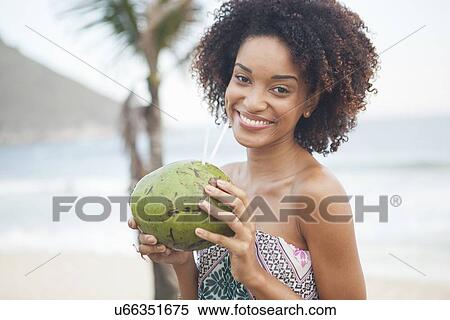 Stock Photography - "Portrait of young woman drinking coconut milk at beach, Rio De Janeiro, Brazil". Fotosearch