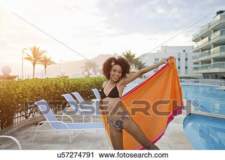 Stock Image - "Portrait of young woman holding up sarong poolside, Rio De Janeiro, Brazil". Fotosearch