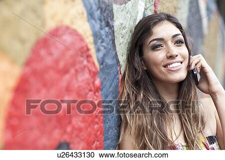 "Portrait of young woman, leaning against wall, using mobile phone, smiling" View Large Photo Image Stock Image - "Portrait of young woman, leaning against wall, using mobile phone, smiling". Fotosearch