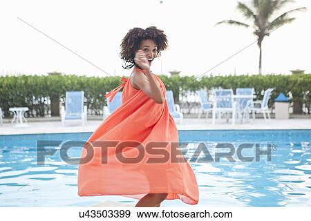 Stock Photo - "Portrait of young woman twirling in orange dress at hotel poolside, Rio De Janeiro, Brazil". Fotosearch