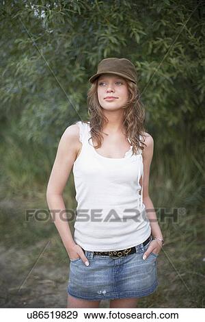 Stock Photo - Portrait of young woman wearing cap with hands in pockets. Fotosearch