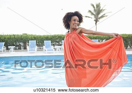 Stock Photography - "Portrait of young woman wearing orange dress at hotel poolside, Rio De Janeiro, Brazil". Fotosearch