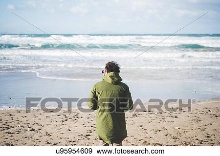 Stock Photo - "Rear view of man looking out to sea from windy beach, Sorso, Sassari, Sardinia, Italy". Fotosearch