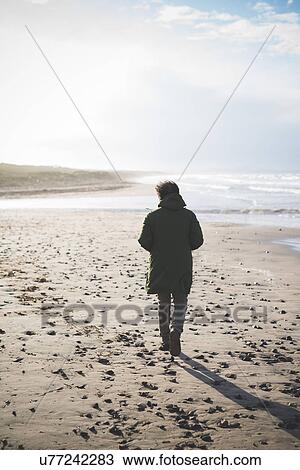 Stock Image - "Rear view of man strolling on windy beach, Sorso, Sassari, Sardinia, Italy". Fotosearch