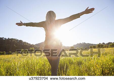 Rear view of mature woman with arms open in meadow at sunset View Large Photo Image Picture - Rear view of mature woman with arms open in meadow at sunset. Fotosearch