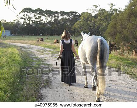 Stock Photography - Rear view of teenage girl leading grey horse. Fotosearch