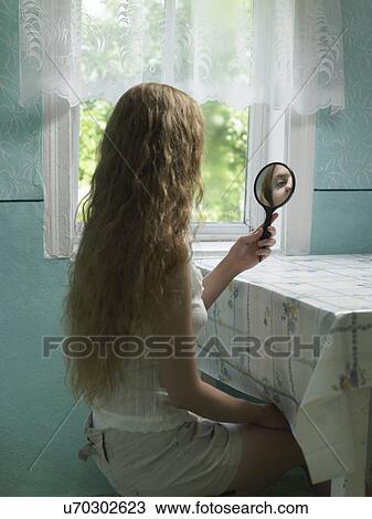 Reflection of young woman looking in hand mirror in kitchen View Large Photo Image Stock Image - Reflection of young woman looking in hand mirror in kitchen. Fotosearch