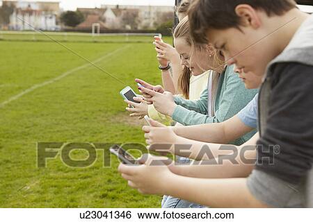 Row of five boys and girls reading smartphone text messages at football pitch View Large Photo Image Stock Photograph - Row of five boys and girls reading smartphone text messages at football pitch. Fotosearch