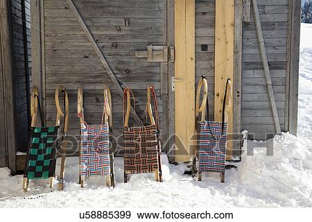 Stock Photo - Row of four sledges leaning against log cabin. Fotosearch