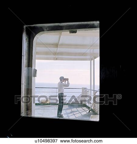 Stock Photo - Sailor using binoculars on container ship at sea. Fotosearch
