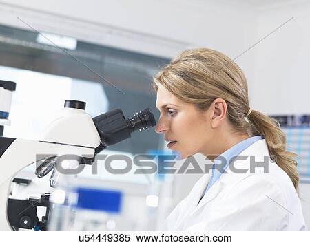Stock Photography - Scientist viewing sample on glass slide through microscope for medical testing. Fotosearch