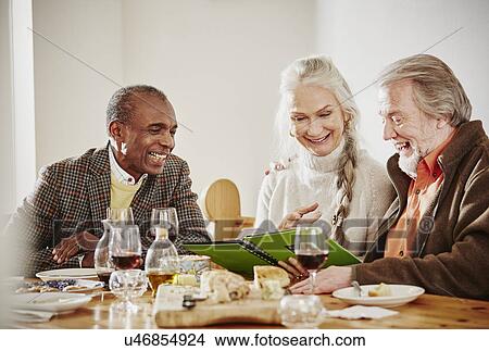 Senior friends looking at book at dinner View Large Photo Image Picture - Senior friends looking at book at dinner. Fotosearch