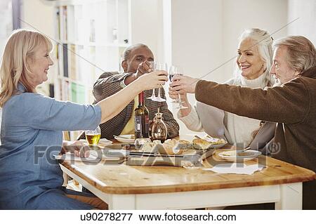 Senior friends making a toast at dinner table View Large Photo Image Stock Photo - Senior friends making a toast at dinner table. Fotosearch