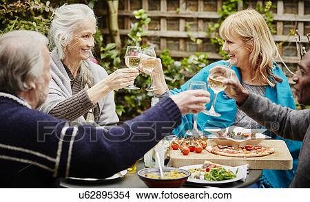 Senior friends making a toast during meal in garden View Large Photo Image Picture - Senior friends making a toast during meal in garden. Fotosearch