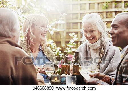Stock Image - Senior friends playing cards in garden. Fotosearch