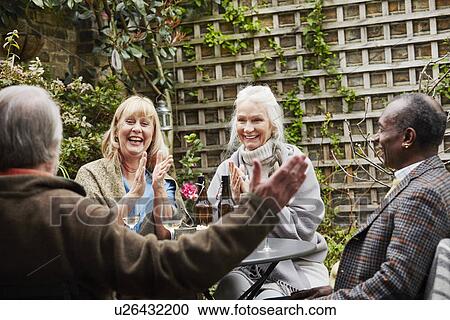 Stock Image - Senior friends sitting in garden talking. Fotosearch