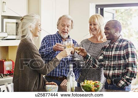 Picture - Senior friends toasting with wine in kitchen. Fotosearch