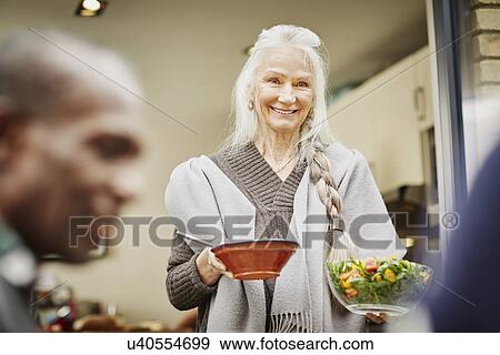 Stock Photo - Senior woman carrying bowls of salad outside. Fotosearch