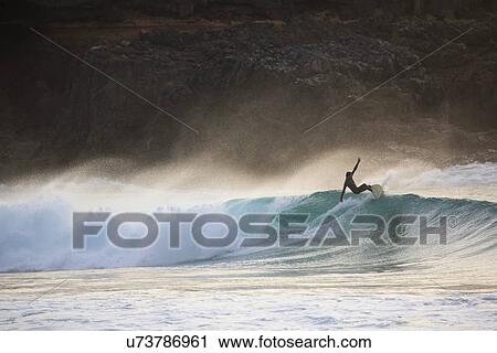 Stock Image - "Silhouetted young man surfing wave at sunset, Fuerteventura, Spain". Fotosearch