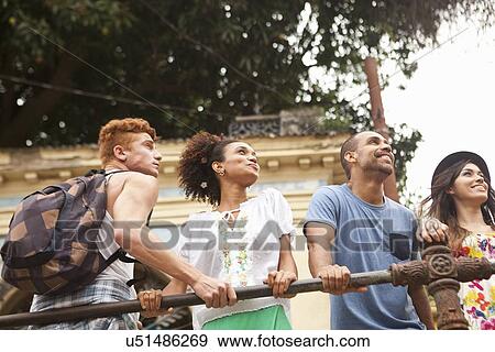 "Small group of friends holding onto railing, smiling, low angle view" View Large Photo Image Stock Photo - "Small group of friends holding onto railing, smiling, low angle view". Fotosearch
