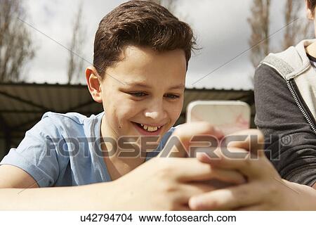 Picture - Smiling boy reading smartphone text message. Fotosearch
