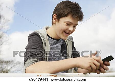 Stock Image - Smiling teenage boy reading smartphone text message. Fotosearch