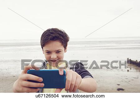 Picture - "Smiling teenage boy taking smartphone selfie at seaside, Southend on Sea, Essex, UK". Fotosearch