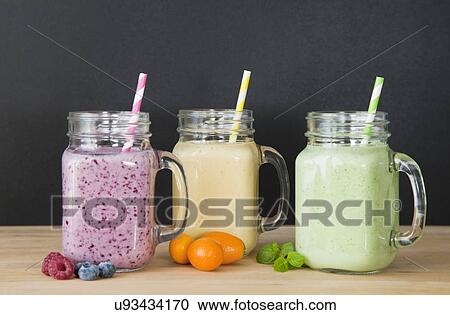 Stock Image - Still life of three fresh smoothies and fruit. Fotosearch