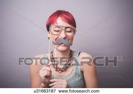 Studio portrait of young woman holding up mustache and spectacles in front of face View Large Photo Image Stock Photo - Studio portrait of young woman holding up mustache and spectacles in front of face. Fotosearch