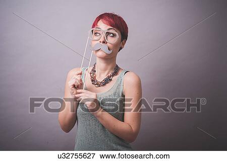 Stock Photo - Studio portrait of young woman holding up spectacles and mustache in front of face. Fotosearch