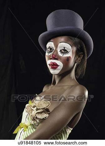 Stock Photography - Studio portrait of young woman in clown face paint wearing top hat. Fotosearch