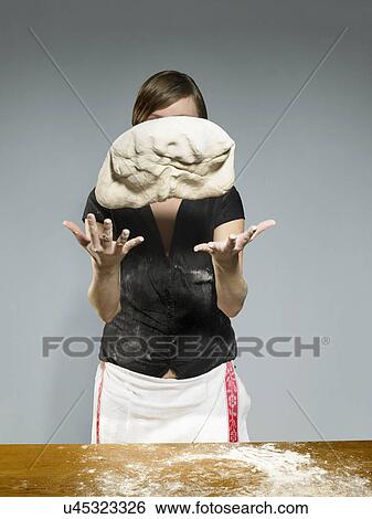Stock Photograph - Studio portrait of young woman throwing bread dough mid air. Fotosearch