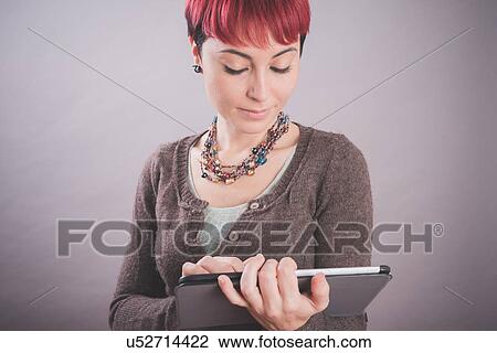 Stock Image - Studio portrait of young woman with short pink hair using touchscreen on digital tablet. Fotosearch