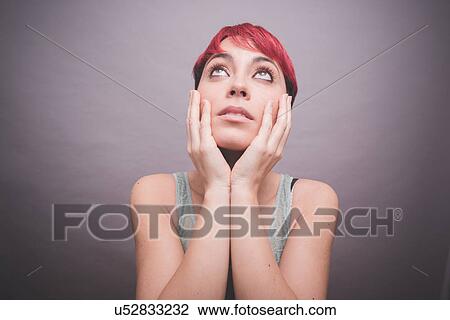 Stock Image - Studio portrait of young woman with short pink hair with hands on cheeks. Fotosearch